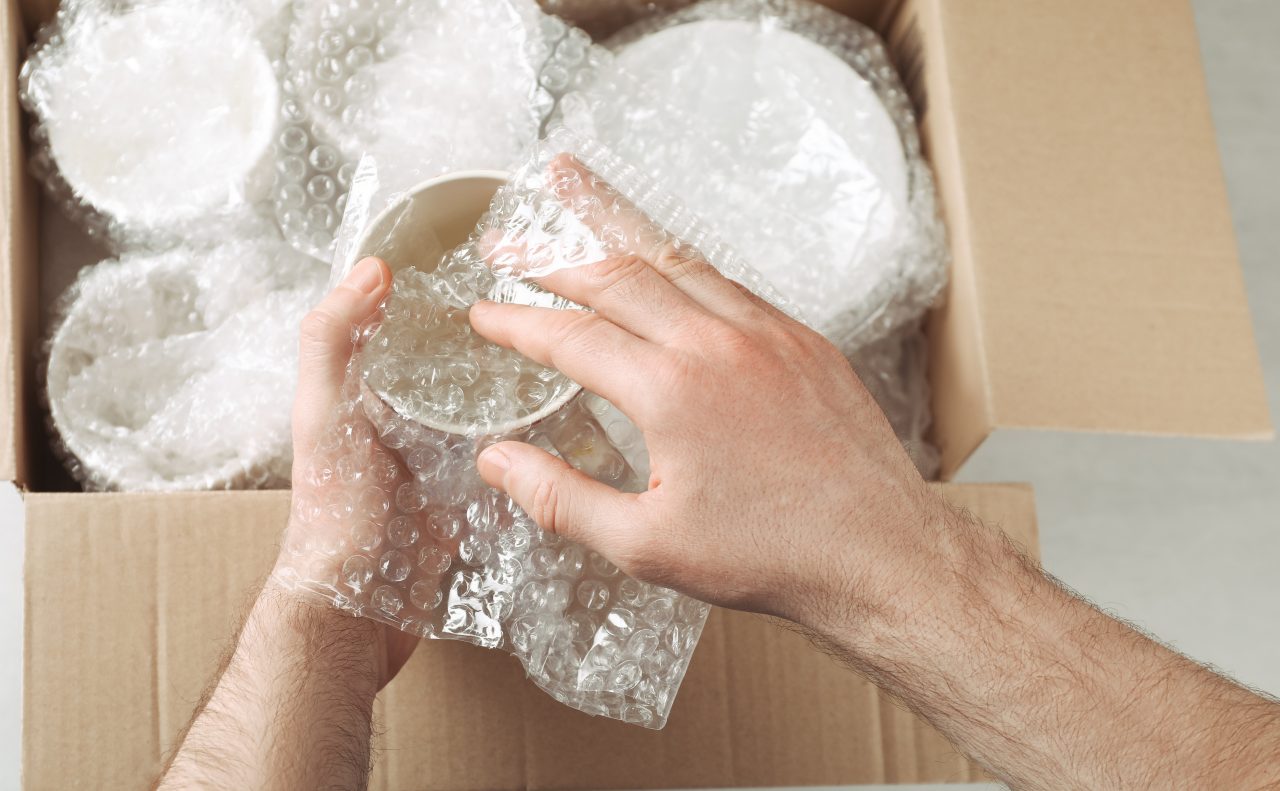 Man covering ceramic dishware with bubble wrap, closeup