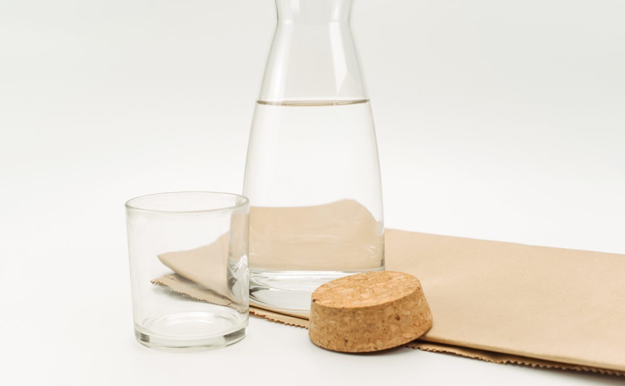 glass flask filled with pure clean water on a white and food paper background with text space